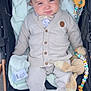 baby, child, stroller, blanket, plush_toy, cardigan, bow_tie, shoes, pants, soft_toy, beige_clothing, infant, cute, outdoor, person, seated, toy, face, blue_eyes, expression