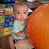 baby, child, orange_ball, play_mat, floor, indoor, toy, curious, sitting, person, wooden_floor, colorful, expression, home, infant, clothing, cute, large_ball, playtime, carpet