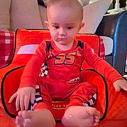 Landon joined the competition — help win amazing prizes! baby, child, toddler, red_clothing, sitting, indoor, cushion, sofa, chair, footwear_barefoot, face, head, hand, home_interior, car_seat, curious, young_child, person, plush, comfort