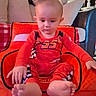 baby, child, toddler, red_clothing, sitting, indoor, cushion, sofa, chair, footwear_barefoot, face, head, hand, home_interior, car_seat, curious, young_child, person, plush, comfort