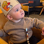 Raphaël participe au concours pour gagner de l'argent avec cette photo : baby, child, paper_crown, highchair, wooden_table, sweater, beaded_clip, indoor, restaurant, portrait, wide_eyes, curious, seat, chair, face, skin, gaze, cute, table, decor