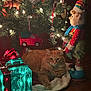 cat, christmas_lights, christmas_tree, cozy, decorations, doll, festive, gift_box, green, holiday, holiday_decor, indoor, lights, orange_cat, ornaments, plush_toy, red, relaxing_cat, toy_car, wood_floor