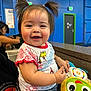Juliet is registered to the contest to win money with this photo: toddler, child, smiling, pigtails, plush_toy, indoor, blue_wall, green_door, shorts, tshirt, happy, person, cute, seated, toy, colorful, face, portrait, young_child, casual_clothing