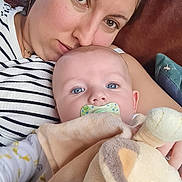 Arthur participe au concours pour gagner de l'argent avec cette photo : woman, baby, infant, child, pacifier, plush_toy, sofa, couch, blanket, striped_shirt, portrait, closeup, brown_hair, blue_eyes, holding, cuddle, relaxing, indoor, soft_toy, family