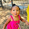 toddler, child, outdoor, playground, fence, sunlight, pacifier, pink_top, yellow_shorts, wood_chips, happy, smiling, person, daylight, cute, young_child, nature, park, casual_clothing, standing