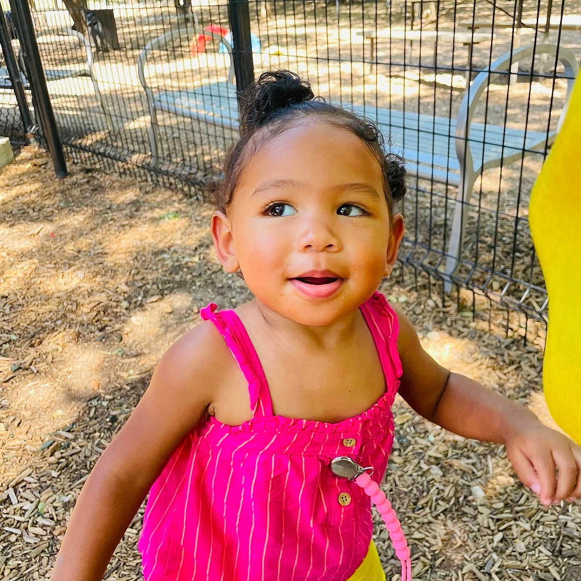 Xola joined the competition — help win amazing prizes! toddler, child, outdoor, playground, fence, sunlight, pacifier, pink_top, yellow_shorts, wood_chips, happy, smiling, person, daylight, cute, young_child, nature, park, casual_clothing, standing