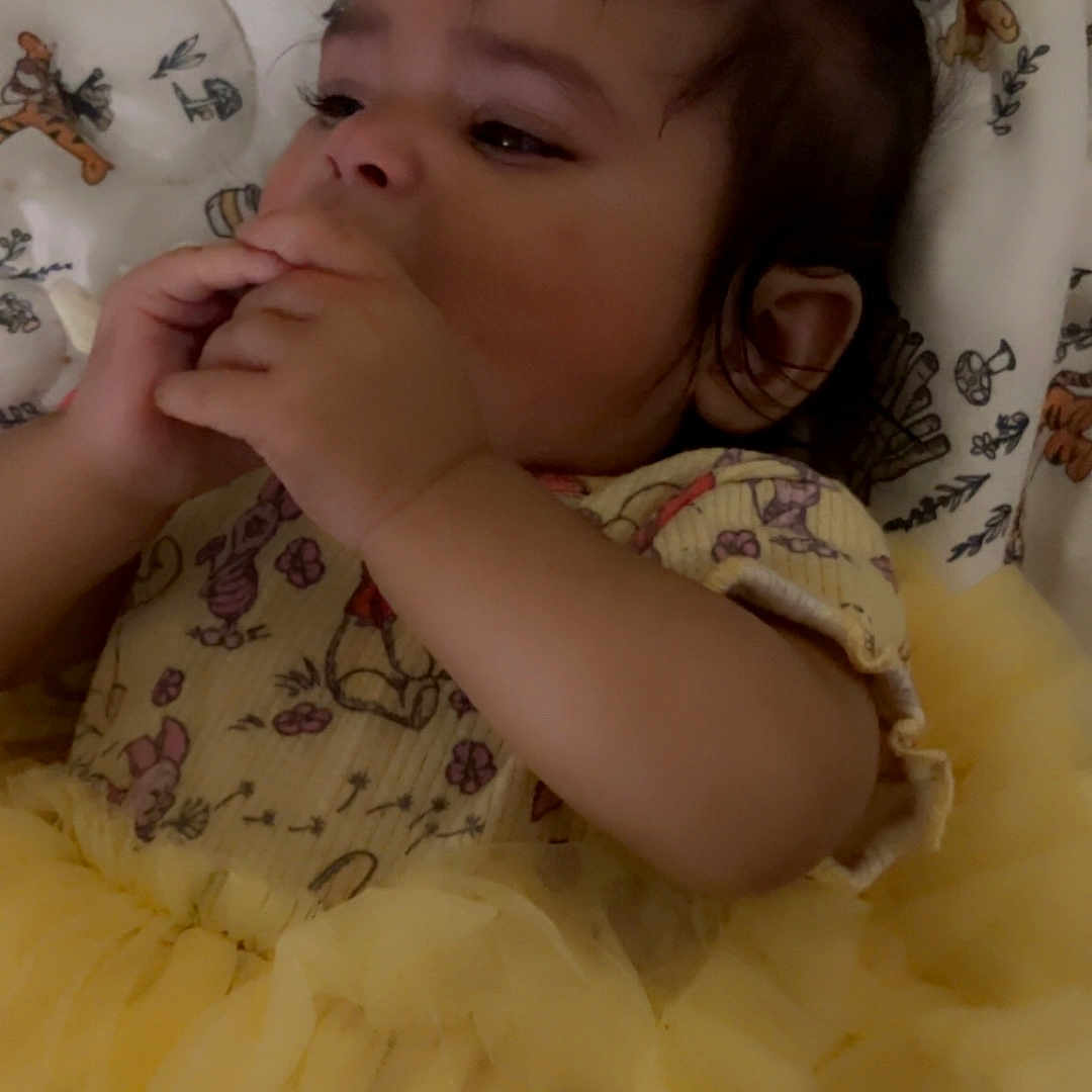 Nahomy is registered to the contest to win money with this photo: animal_print, baby, blanket, child, cute, dark_hair, expressive, face, hand, indoors, infant, lying_down, pattern, portrait, resting, small_hands, soft_lighting, tulle_skirt, yellow_dress, young_child