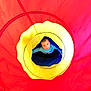 Waylen is registered to the contest to win money with this photo: child, toddler, face, person, play_tunnel, toy, colorful, red, yellow, blue, circle, top_down, looking_up, curious, indoor, fabric, playtime, portrait, bright, sweater