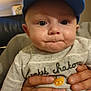 baby, child, cap, blue_cap, person, adult_hands, indoor, clothing, grey_outfit, cute, face, expression, close_up, holding, portrait, young_child, cat_design, human, headwear, infant