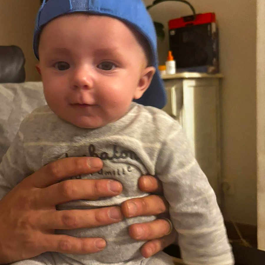 Andrea a rejoint le concours — aidez-le/la à gagner de superbes lots ! baby, blue_cap, cabinet, cap, casual, child, clothing, cute, face, furniture, hands, home, indoor, infant, person, plant, portrait, sitting, smile, young