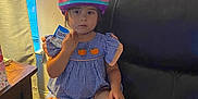 Evelyn is registered to the contest to win money with this photo: child, girl, helmet, blue_dress, pumpkin_design, snack, couch, leather, window, curtain, tissue, indoor, sitting, thoughtful, person, footwear, pink_helmet, table, daylight, casual