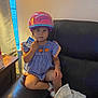 child, girl, helmet, blue_dress, pumpkin_design, snack, couch, leather, window, curtain, tissue, indoor, sitting, thoughtful, person, footwear, pink_helmet, table, daylight, casual