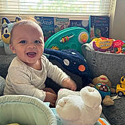 Xander joined the competition — help win amazing prizes! baby, smiling, indoor, toys, stuffed_animal, books, window, blinds, couch, child, happy, play, soft_toy, colorful, infant, person, cute, cozy, daylight, living_room