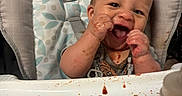 Xander is registered to the contest to win money with this photo: baby, high_chair, messy, food, happy, smiling, toy, infant, face, hands, feeding, child, indoor, playful, cute, expression, seat, clothing, table, meal