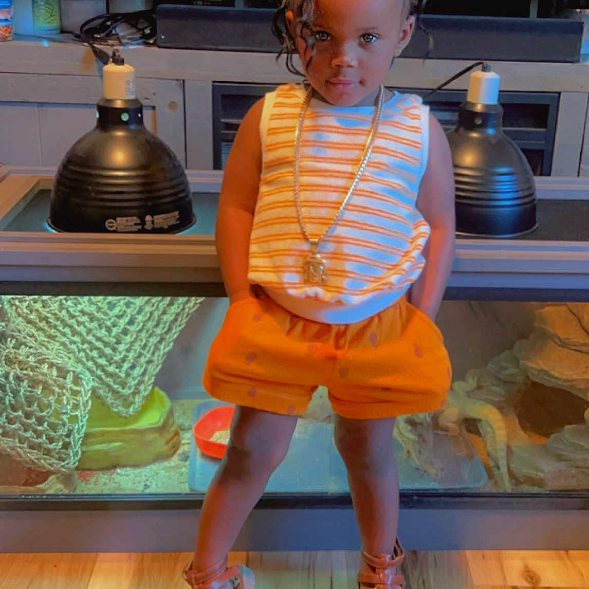 Janiyah is registered to the contest to win money with this photo: accessories, child, clothing, face, female, footwear, furniture, girl, head, indoors, jewelry, necklace, person, photography, portrait, sandal, shoe, shorts, table, wood