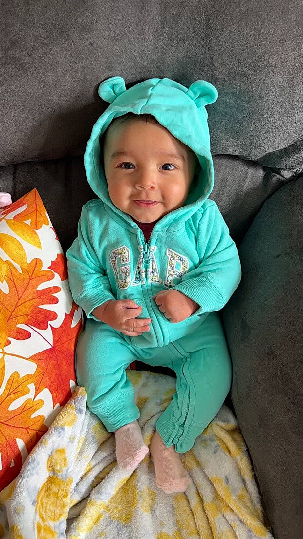 Jaylani is registered to the contest to win money with this photo: baby, baby_toddler_clothing, cap, child, comfort, face, fashion_accessory, grass, happy, head, headwear, hood, hoodie, joy, linens, person, product, sitting, sleeve, smile