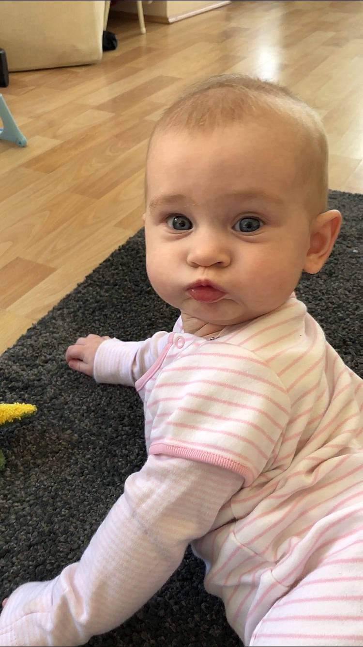 Lacie is registered to the contest to win money with this photo: baby, cheek, child, chin, eye, face, floor, flooring, head, leg, lip, mouth, nose, person, pink, sitting, skin, smile, toddler, wood