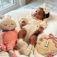 Vivian joined the competition — help win amazing prizes! baby, infant, one_month, blanket, knitted_doll, bunny_toy, headband, bow, white_socks, wooden_sign, soft_toys, window, natural_light, indoor, cute, newborn, clothing, baby_pose, bed, curious