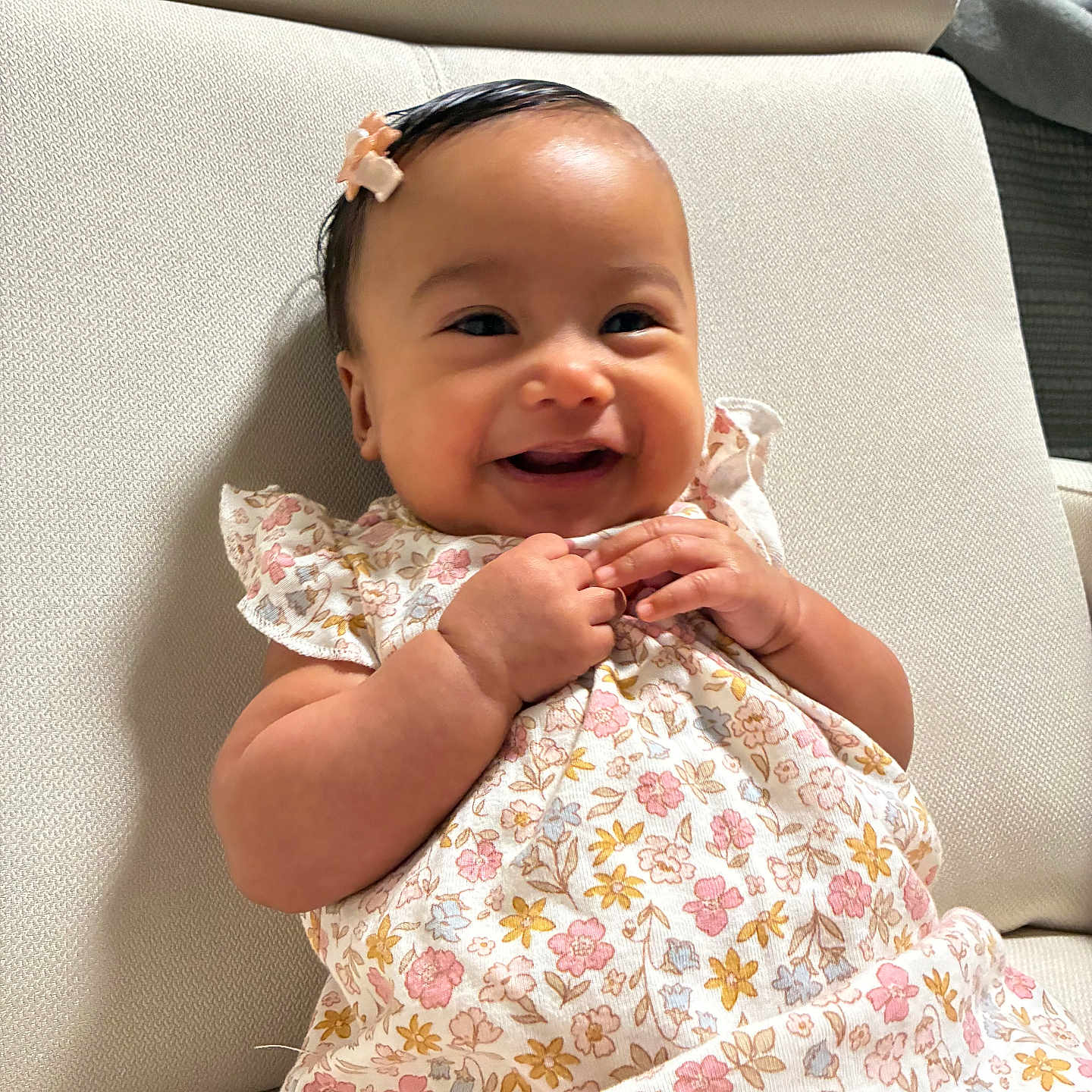 Vivian is registered to the contest to win money with this photo: baby, child, comfortable, couch, cute, dress, face, floral_pattern, furniture, hair_clip, hands, happy, indoor, infant, person, portrait, sitting, skin, smiling, young