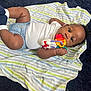 baby, infant, toy, blanket, striped_blanket, lying_down, curious, chewing, clothing, white_shirt, blue_diaper, socks, indoor, carpet, black_carpet, hand, face, eyes, cute, child