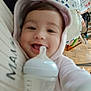 baby, bottle, hoodie, smile, indoor, floor, wooden_floor, baby_gear, person, face, child, clothing, toy, feeding, happy, cute, infant, closeup, hand, warm