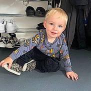 Kaylan is registered to the contest to win money with this photo: black_pants, blond_hair, blue_eyes, casual, child, clothing, construction_pattern, cute, face, floor, hand, indoor, jacket, person, shoe_rack, shoes, smiling, sneakers, sweater, toddler