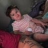 arm, baby, bed, blanket, bottle, child, cozy, curly_hair, family, indoor, intimate, person, portrait, relaxing, sleeping, smile, striped_clothing, stuffed_animal, tattoo, toddler