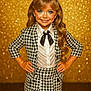 child, girl, smile, posing, bow, blonde_hair, long_hair, fashion, houndstooth, suit, skirt, white_shirt, black_tie, sparkle, glitter, gold_background, portrait, studio, confident, hands_on_hips
