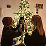 black_and_white_cat, cat, celebration, christmas_tree, cozy, decorations, festive, glasses, happy, holiday, indoor, lights, ornaments, people, sitting, smiling, together, tree_star, warm_lighting, young_adults