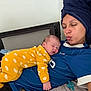 baby, woman, sleeping, yellow_onesie, blue_shirt, towel, face, indoor, cozy, cute, child, person, resting, pacifier, bed, blanket, relaxing, skin, headwear, portrait