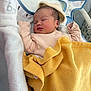 newborn, baby, sleeping, blanket, hat, infant, cozy, soft, pink_clothing, yellow_blanket, baby_carrier, peaceful, resting, face, head, person, child, indoors, comfort, cushion