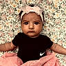 baby, infant, child, headband, bow, pink_tutu, black_onesie, nike_logo, floral_blanket, lying_down, wide_eyes, serious_expression, cute, fashion, portrait, indoors, soft_lighting, skin, person, clothing