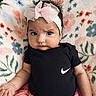 baby, infant, headband, bow, clothing, black_onesie, pink_skirt, floral_blanket, cute, portrait, child, toddler, fashion, expression, indoor, person, face, sitting, colorful, soft_texture