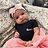 baby, infant, pink_bow, black_onesie, pink_tutu, blanket, floral_pattern, headband, indoor, living_room, couch, curious_expression, person, child, cute, soft_lighting, portrait, toy, toddler, clothing