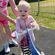 Poppy joined the competition — help win amazing prizes! baby, child, playground, spring_rocker, outdoor, smiling, person, toy, grass, fence, sunny, footwear, clothing, hands, face, happy, support, adult, park, play