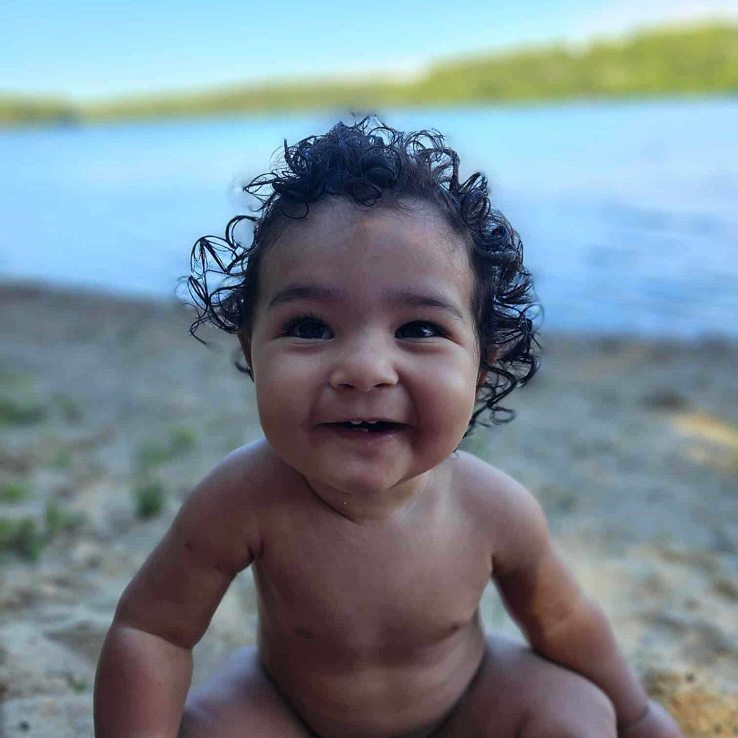 Romeo is registered to the contest to win money with this photo: baby, bare_chest, child, closeup, curly_hair, cute, happy, innocence, lake, nature, outdoor, playful, portrait, sand, sitting, smiling, summer, sunlight, water, young_child
