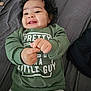 Romeo is registered to the contest to win money with this photo: baby, child, smiling, curly_hair, green_sweatshirt, clothing, bed, gray_pants, lying_down, happy, infant, portrait, indoor, person, cute, hands, face, young_child, text_on_clothing, playful