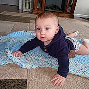Lyric is registered to the contest to win money with this photo: baby, child, blue_eyes, knitted_blanket, carpet, living_room, fireplace, bookshelf, crawling, socks, hoodie, indoor, floor, cute, person, portrait, home, furniture, infant, curious
