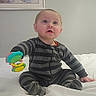Lyric is registered to the contest to win money with this photo: baby, child, striped_pajamas, toy, bed, white_bedspread, indoor, curious, sitting, blue_eyes, pajamas, hand, face, expression, room, wall, painting, modern, floor_lamp, soft_lighting