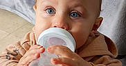 Lyric is registered to the contest to win money with this photo: baby, bottle, blue_eyes, child, clothing, face, hand, hoodie, indoor, person, portrait, skin, sitting, table, toddler, young_child, feeding, cute, closeup, expression