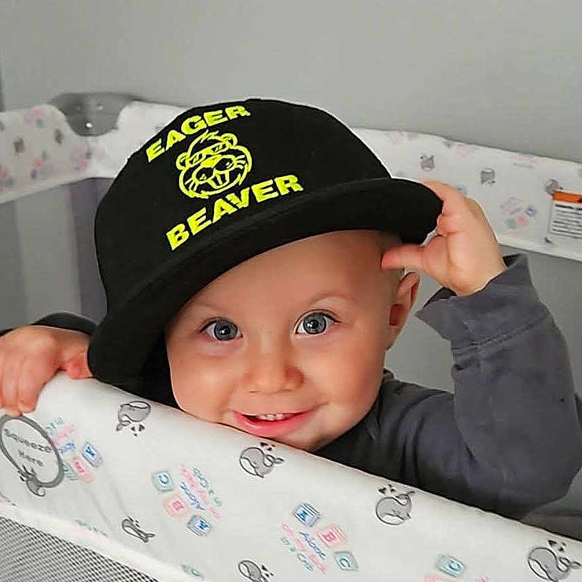Lyric is registered to the contest to win money with this photo: baby, child, cap, hat, crib, smile, blue_eyes, face, hand, clothing, indoor, playful, cute, person, infant, pattern, fabric, headwear, young_child, happy