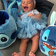 Marilyn is registered to the contest to win money with this photo: baby, child, smiling, blue_dress, headband, plush_toy, stitch, couch, indoor, happy, barefoot, fabric, toy, sitting, cute, infant, playful, person, soft_toys, comfort