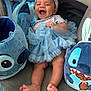 baby, child, smiling, blue_dress, headband, plush_toy, stitch, couch, indoor, happy, barefoot, fabric, toy, sitting, cute, infant, playful, person, soft_toys, comfort