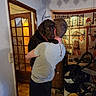 dog, labrador, chocolate_lab, person, hugging, indoor, portrait, pet, companion, brown_dog, collar, large_dog, standing, cuddle, home, doorway, egyptian_art, wall_hanging, cleaning_equipment, household