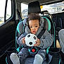 baby, child, car_seat, toddler, soccer_ball, winter_clothing, jacket, seatbelt, car_interior, window, suburban, house, curly_hair, footwear, cozy, safety, curious, indoors, person, transportation