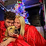 couple, dog, christmas_tree, red_pajamas, holiday, indoor, decorations, lights, white_tree, affection, cuddling, love, festive, smiling, blonde_hair, curly_hair, ornaments, celebration, warm_lighting, home