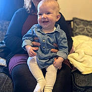 Evelyn-Rose is registered to the contest to win money with this photo: baby, child, couch, cozy, cute, denim_dress, face, family, furniture, hands, happy, holding, home, indoor, person, portrait, seated, smiling, white_tights, woman