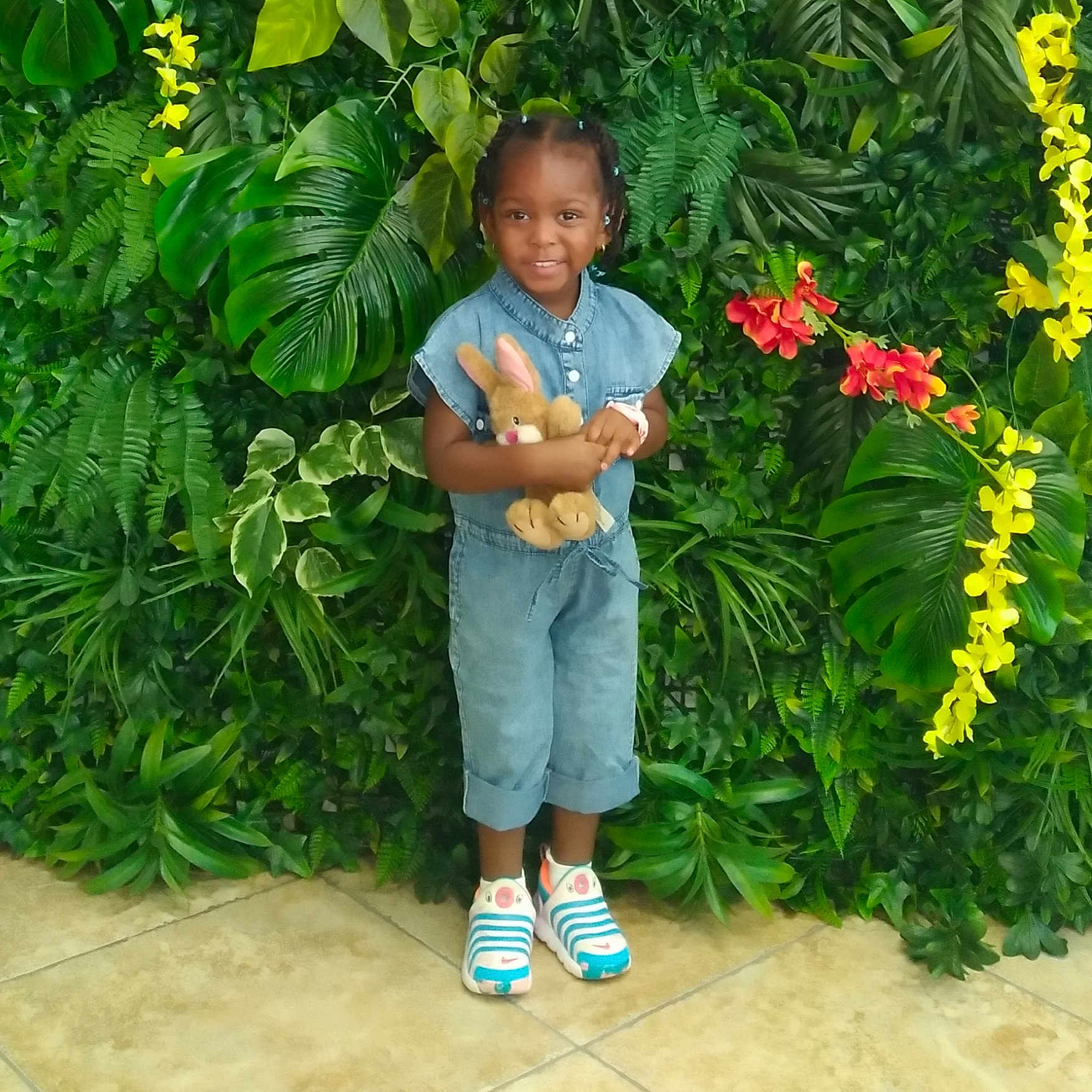 Emeri is registered to the contest to win money with this photo: child, smiling, denim_jumpsuit, plush_toy, bunny, greenery, leaves, flowers, yellow_flowers, red_flowers, sneakers, standing, indoor, portrait, happy, cute, person, hair_beads, tile_floor, colorful