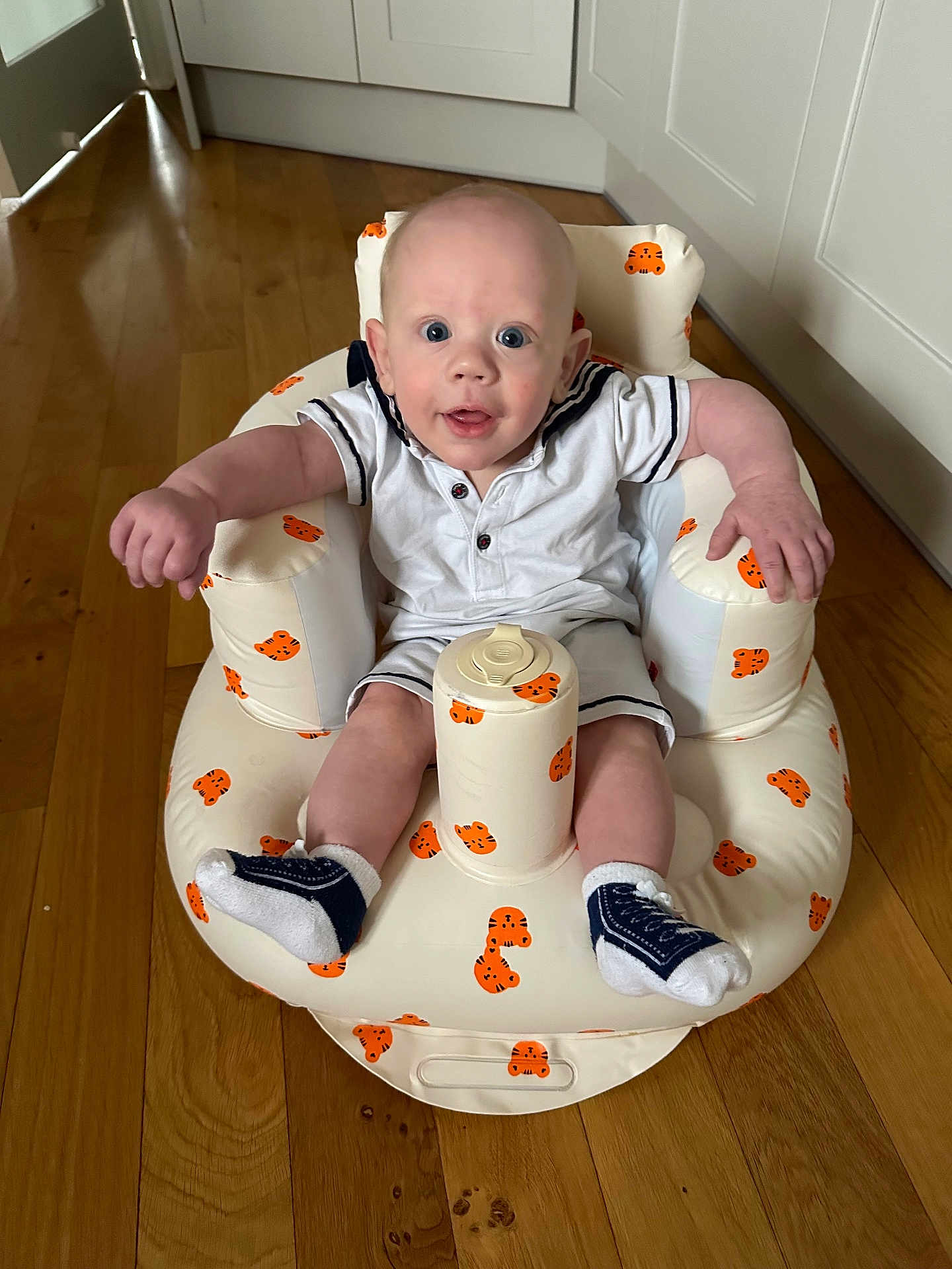 Tiaan is registered to the contest to win money with this photo: baby, child, comfort, curious, cute, expression, face, footwear, home, indoor, infant, inflatable_chair, joyful, person, plush, sitting, socks, tiger_pattern, white_clothing, wooden_floor