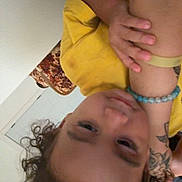 Amir is registered to the contest to win money with this photo: child, toddler, portrait, upside_down, curly_hair, yellow_clothing, smiling, indoor, face, eyes, hands, bracelet, beads, tattoo, bed, blanket, home, close_up, casual, photography